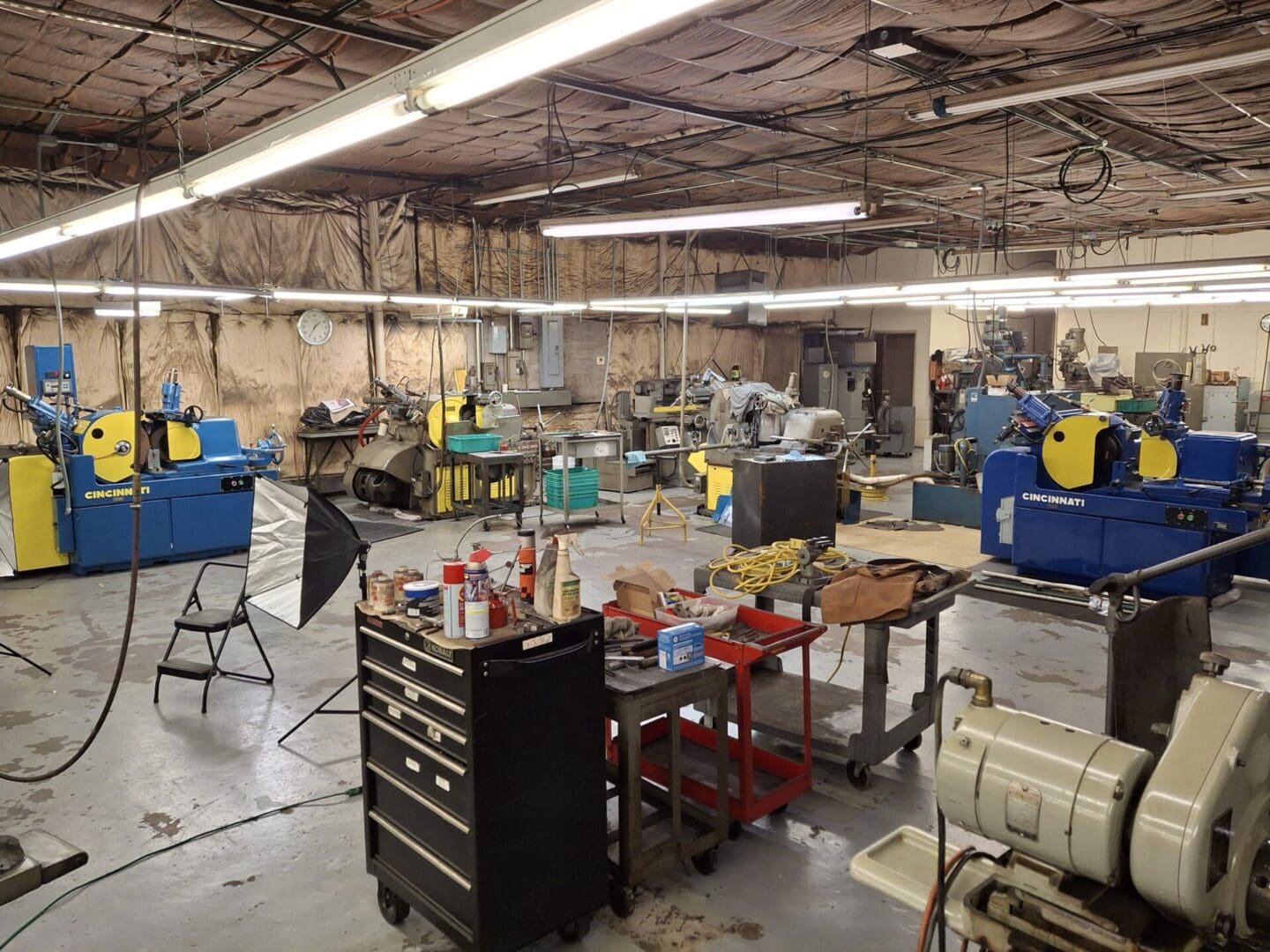 A cluttered workshop with tools and equipment under fluorescent lighting.